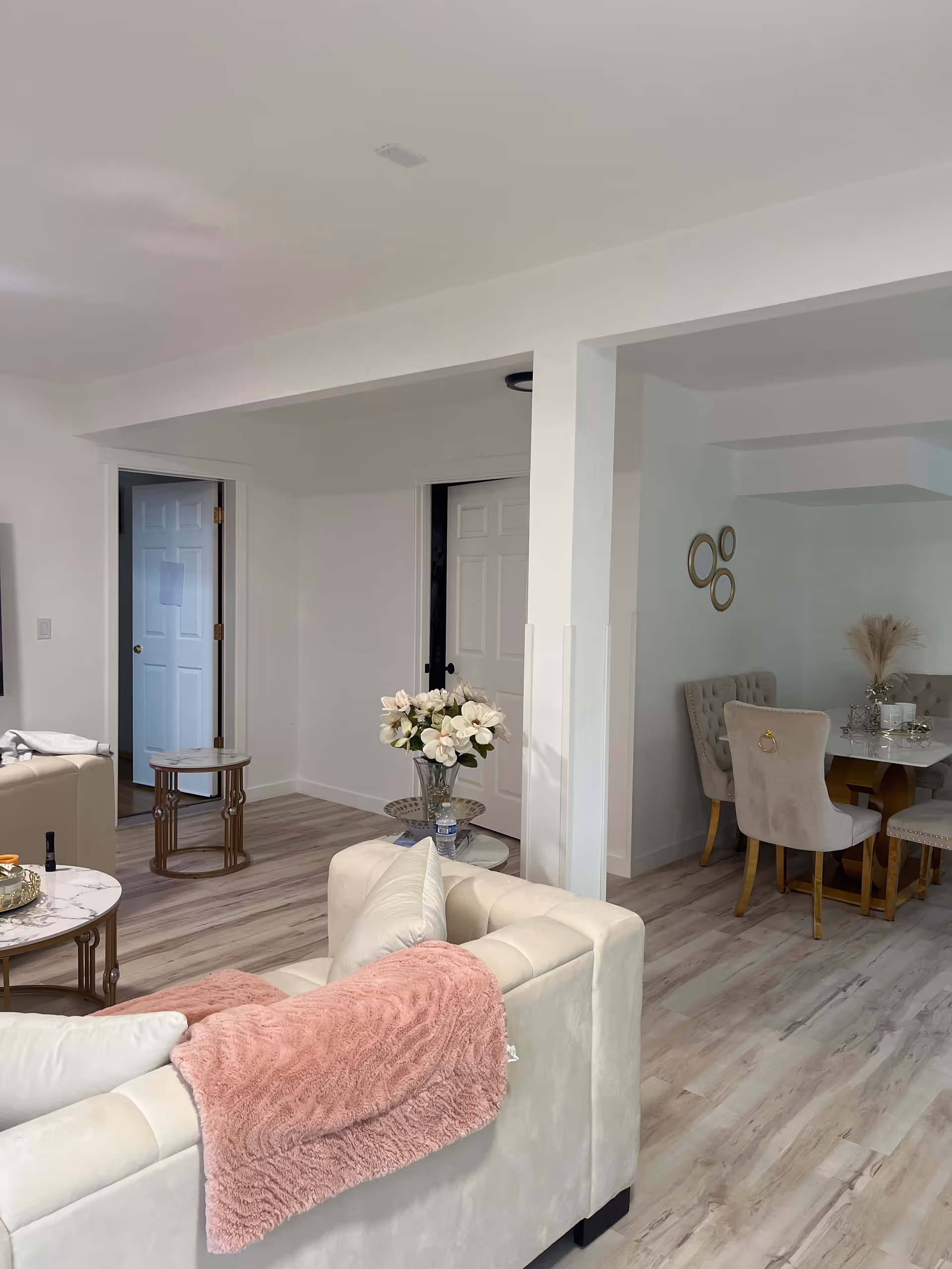 Bright open living area with cream sofa, pink throw, vase of flowers, and dining table.