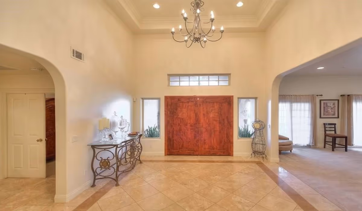 Bright entry foyer with chandeliers, double doors, and decorative console table.