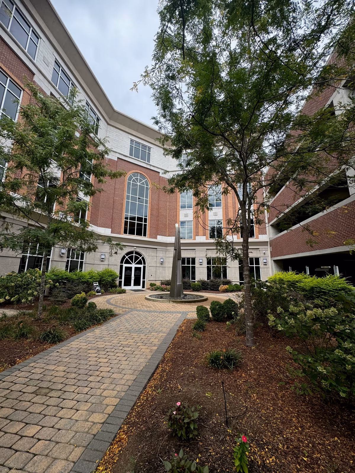 Carepoint senior living courtyard with brick building, arched windows, trees, and a central sculpture.