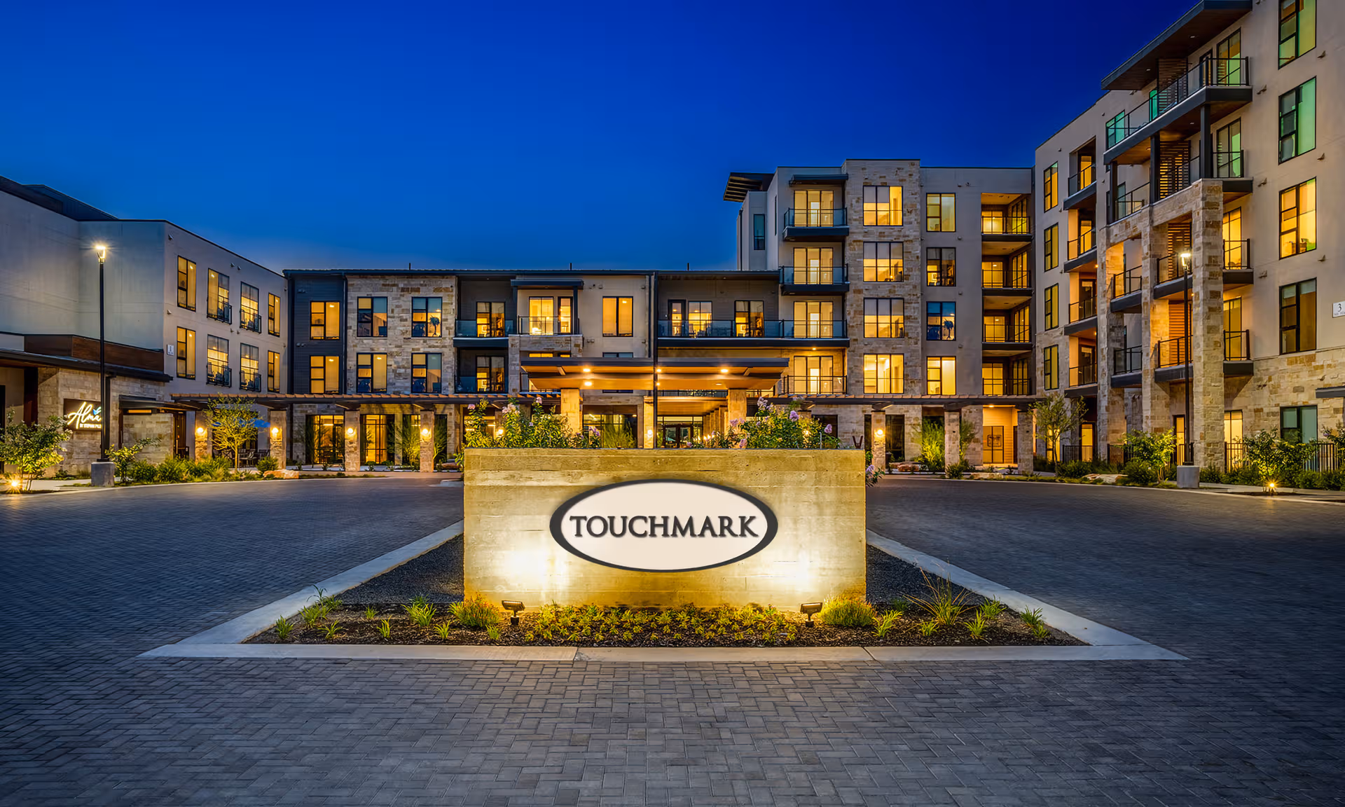 Nighttime exterior view of a modern senior living campus with lit windows and a central sign.