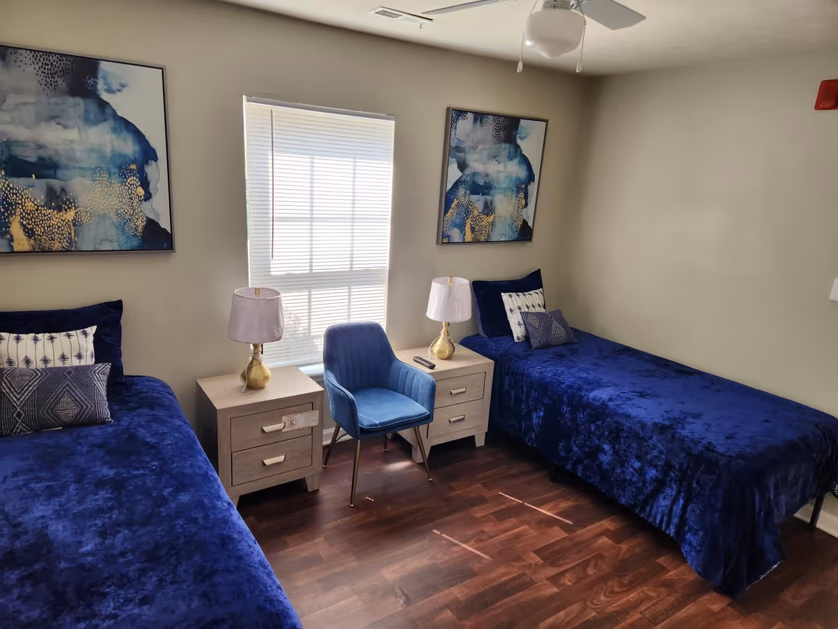Two navy blue twin beds with nightstands, lamps, a blue chair, and abstract wall art.