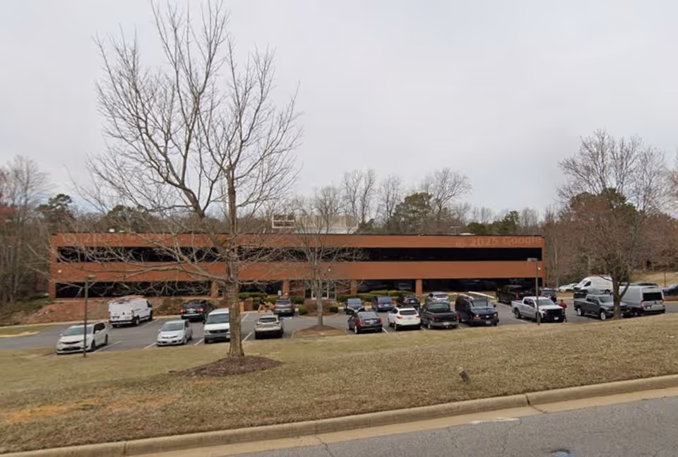 Parking lot in front of a brown brick facility with multiple cars.