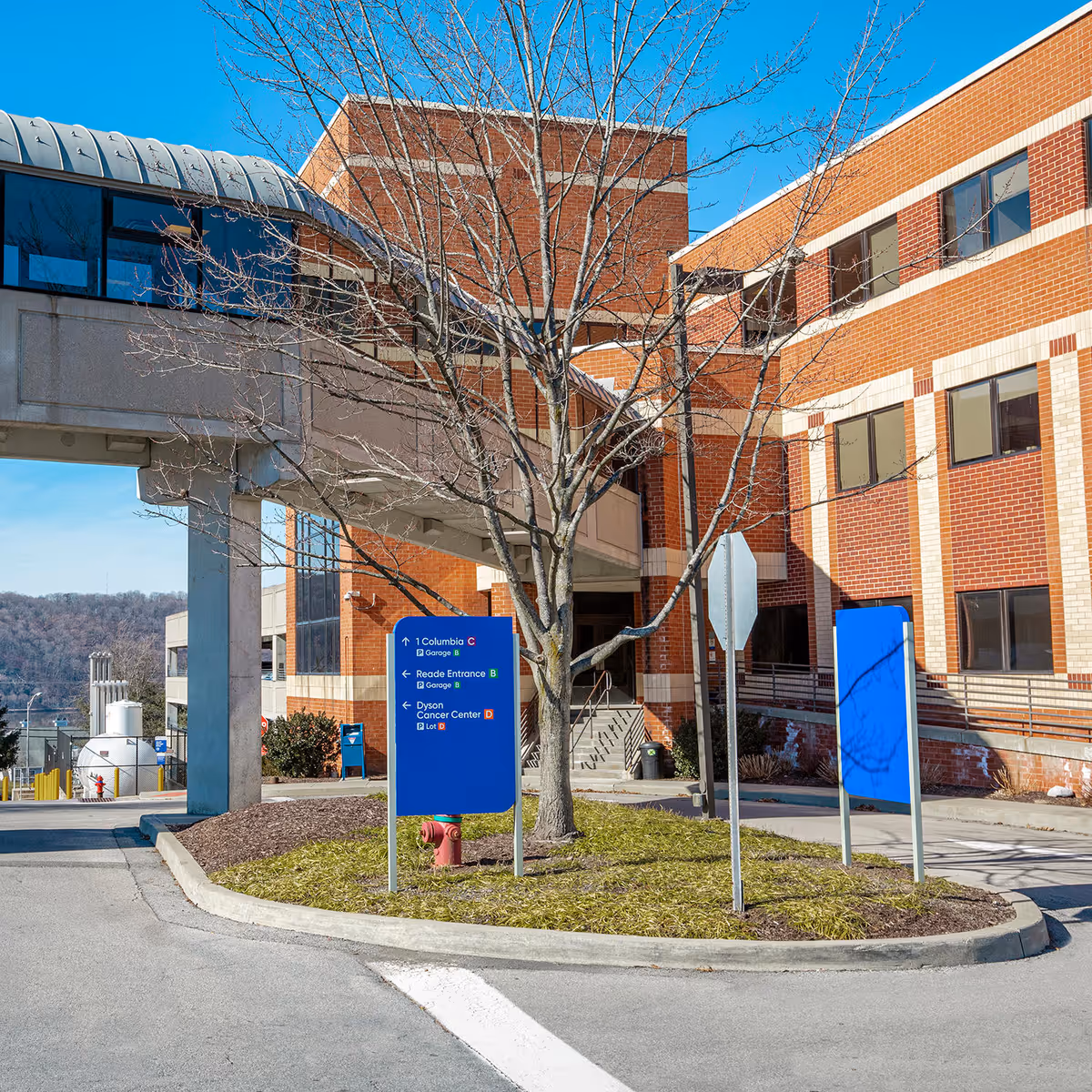 Exterior view of a brick medical facility with blue directional signs and a leafless tree