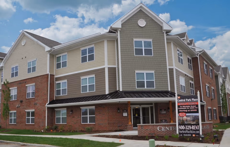 Front view of Central Park Place senior living building with brick base and beige siding.