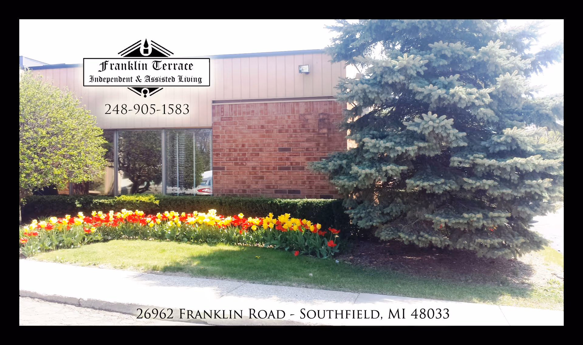 Exterior view of Franklin Terrace with sign, brick facade, trees, and flower bed.