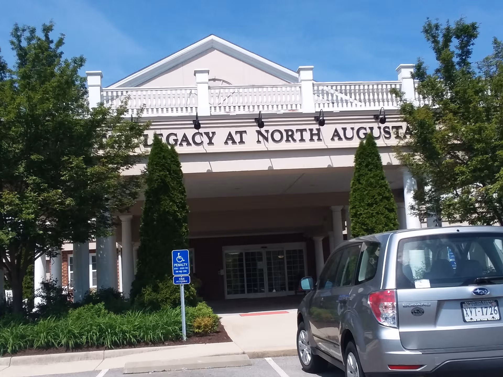 Front view of The Legacy at North Augusta entrance with trees and a parked SUV.