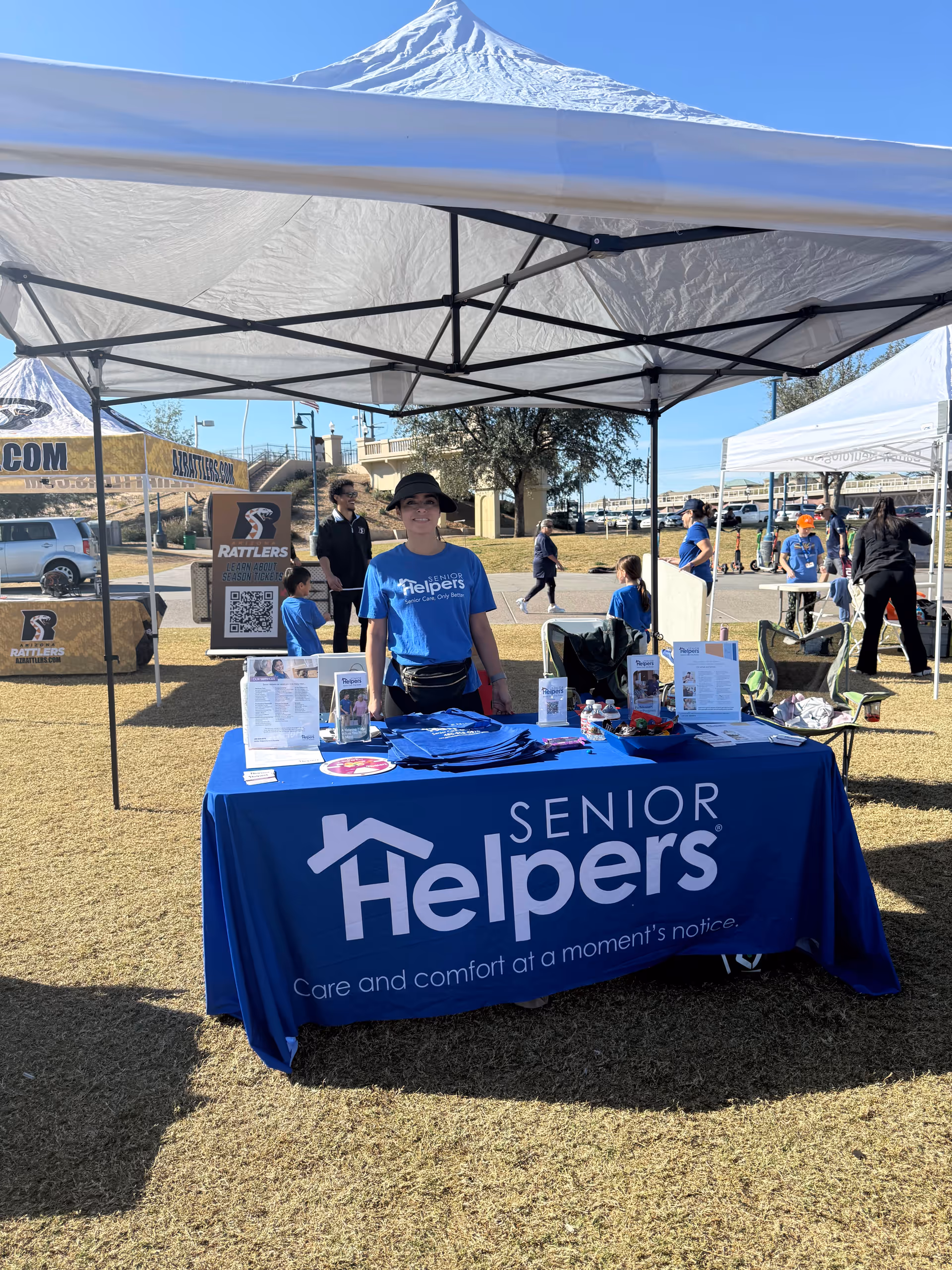Senior Helpers booth under tents at an outdoor event with staff and attendees.