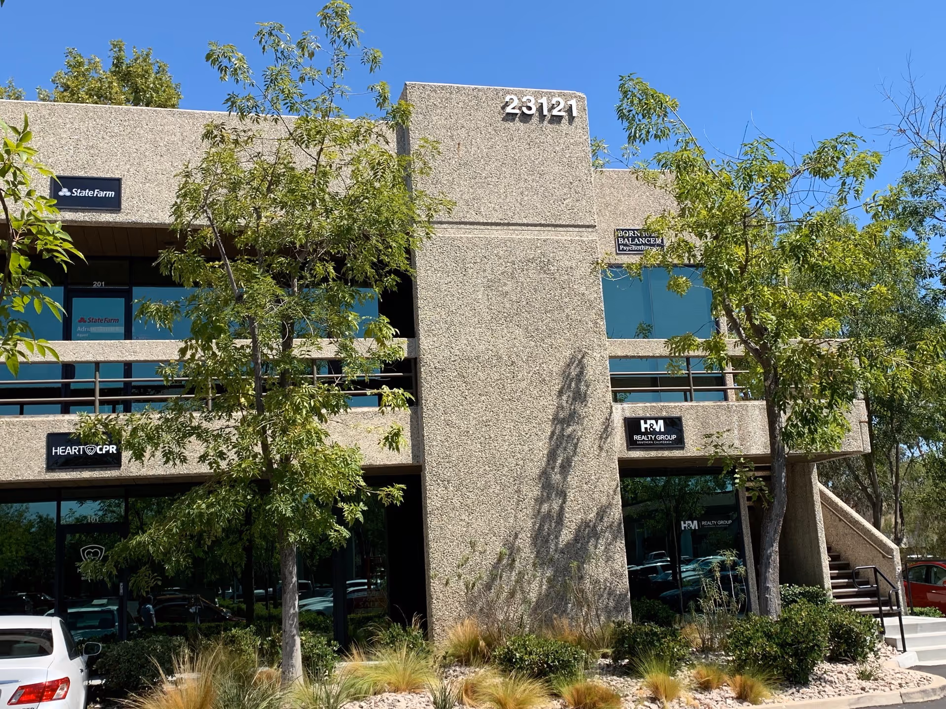 Front view of a beige two-story commercial building with trees and signs.