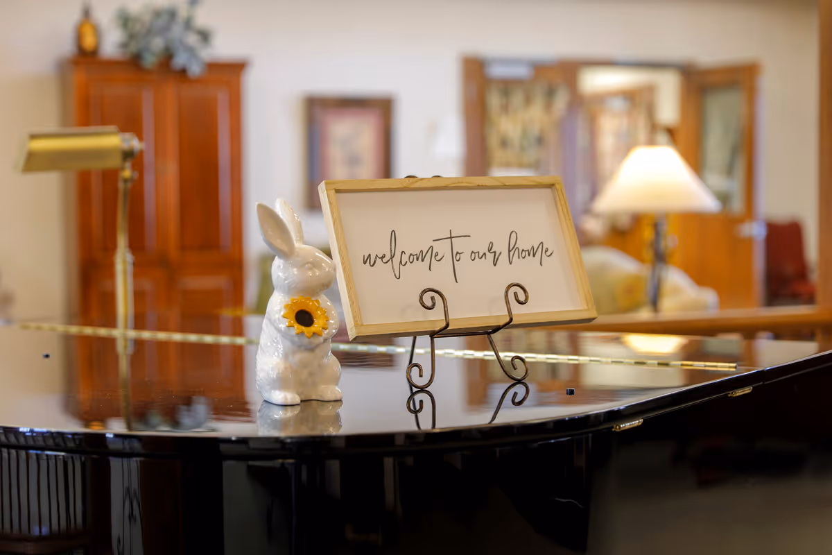 A glossy grand piano with a bunny figurine and welcome sign in a cozy lobby area.
