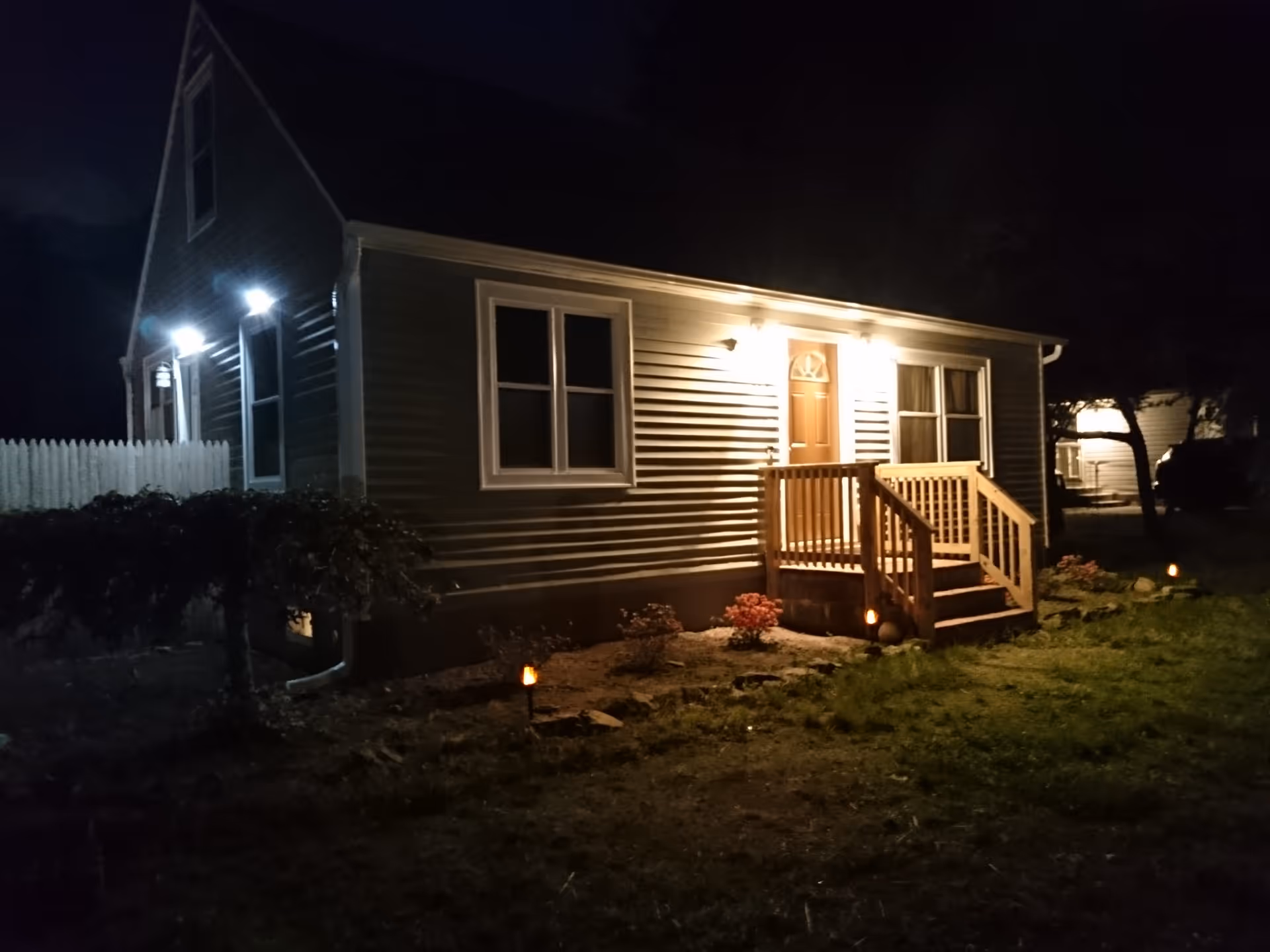 Nighttime exterior of a single-story building with a wooden front porch and illuminated entry.