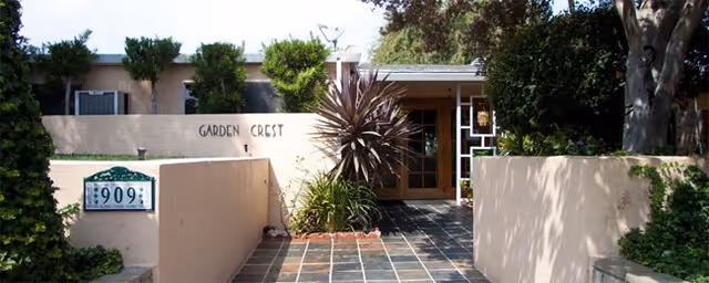 Entrance to Garden Crest senior living, beige exterior walls, tiled path, plants, and signage.