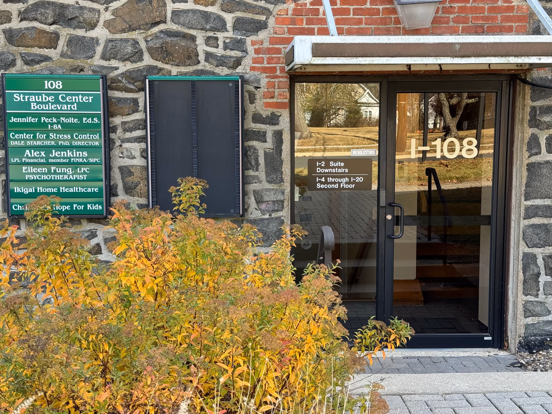 Exterior stone building with glass entrance door and green signage outside.