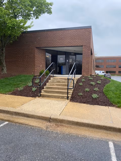 Brick building entrance with stairs, metal railings, and landscaped surrounding plants.
