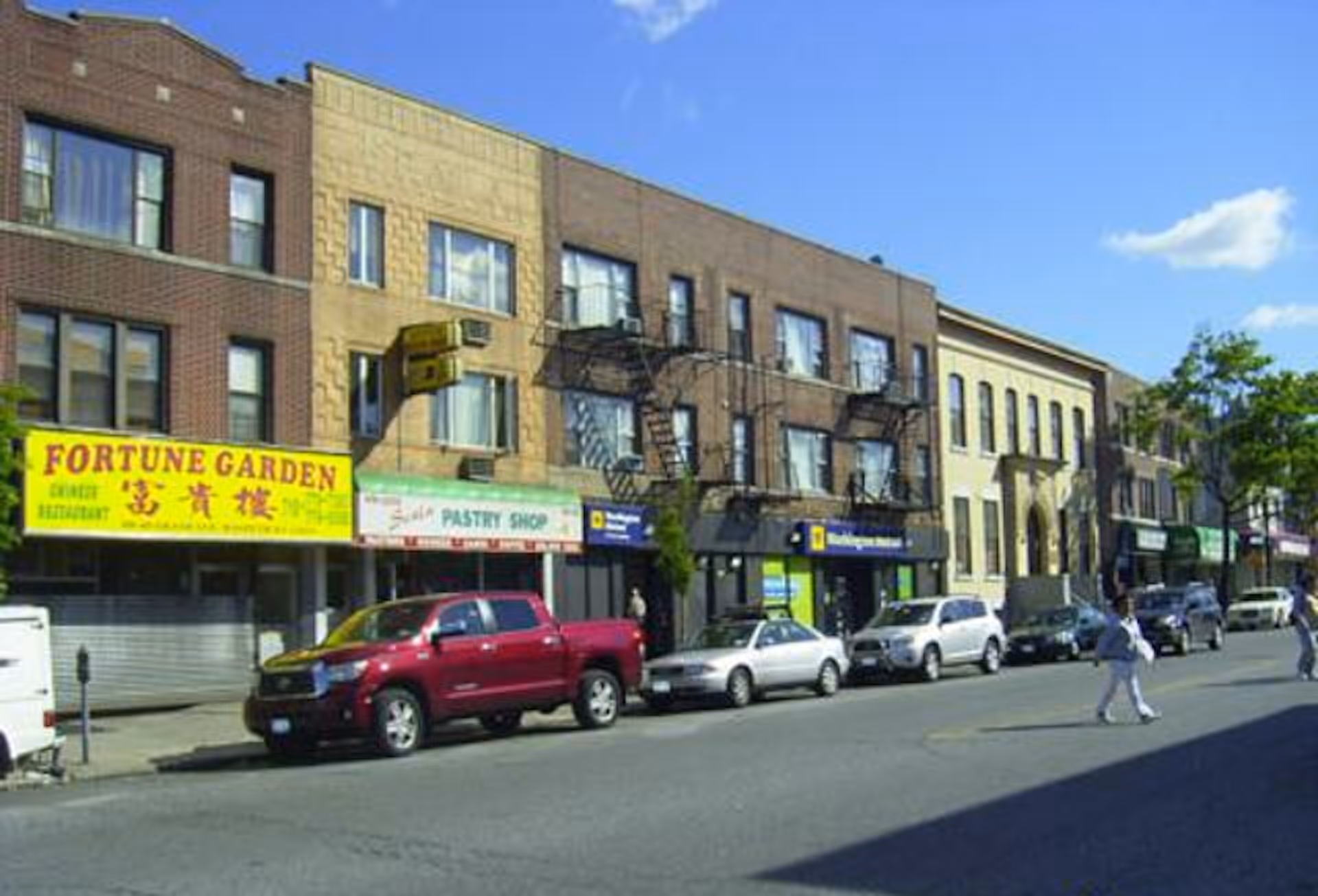 Exterior street view showing brick storefronts, parked cars, and pedestrians.