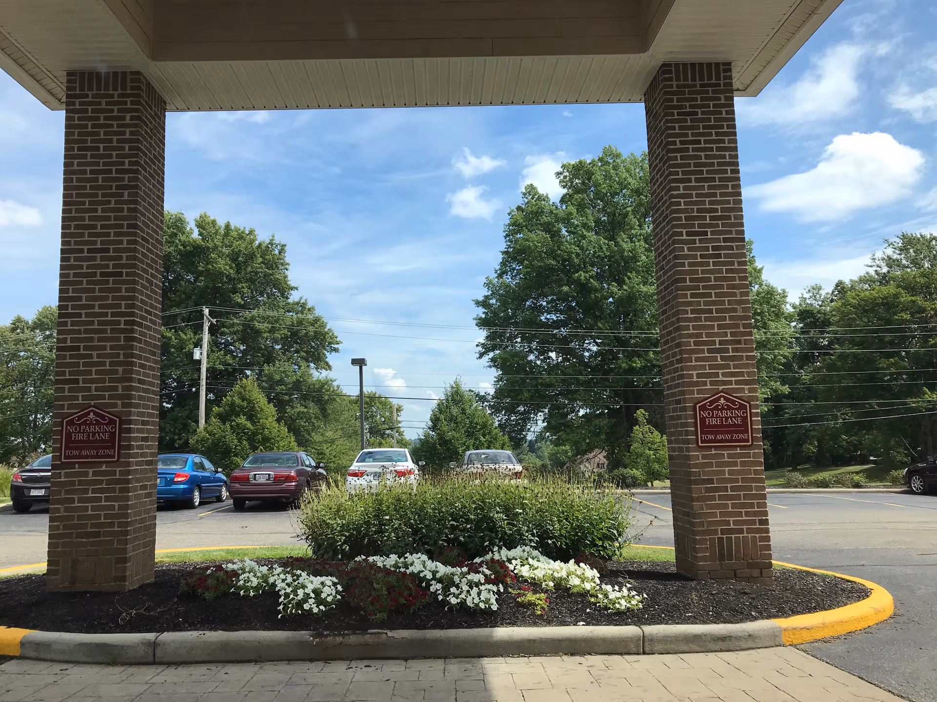 Covered entrance with brick pillars, parked cars, and a landscaped flower bed.