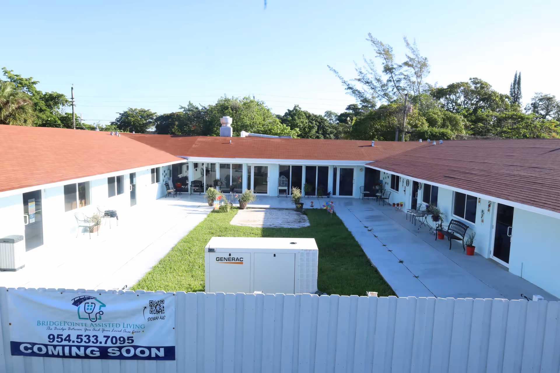 A U-shaped senior living courtyard with green lawn, benches, potted plants, and a banner.