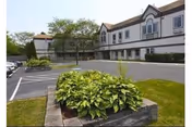 Exterior view of Village House Nursing and Rehabilitation Center with parking and landscaped shrubs.