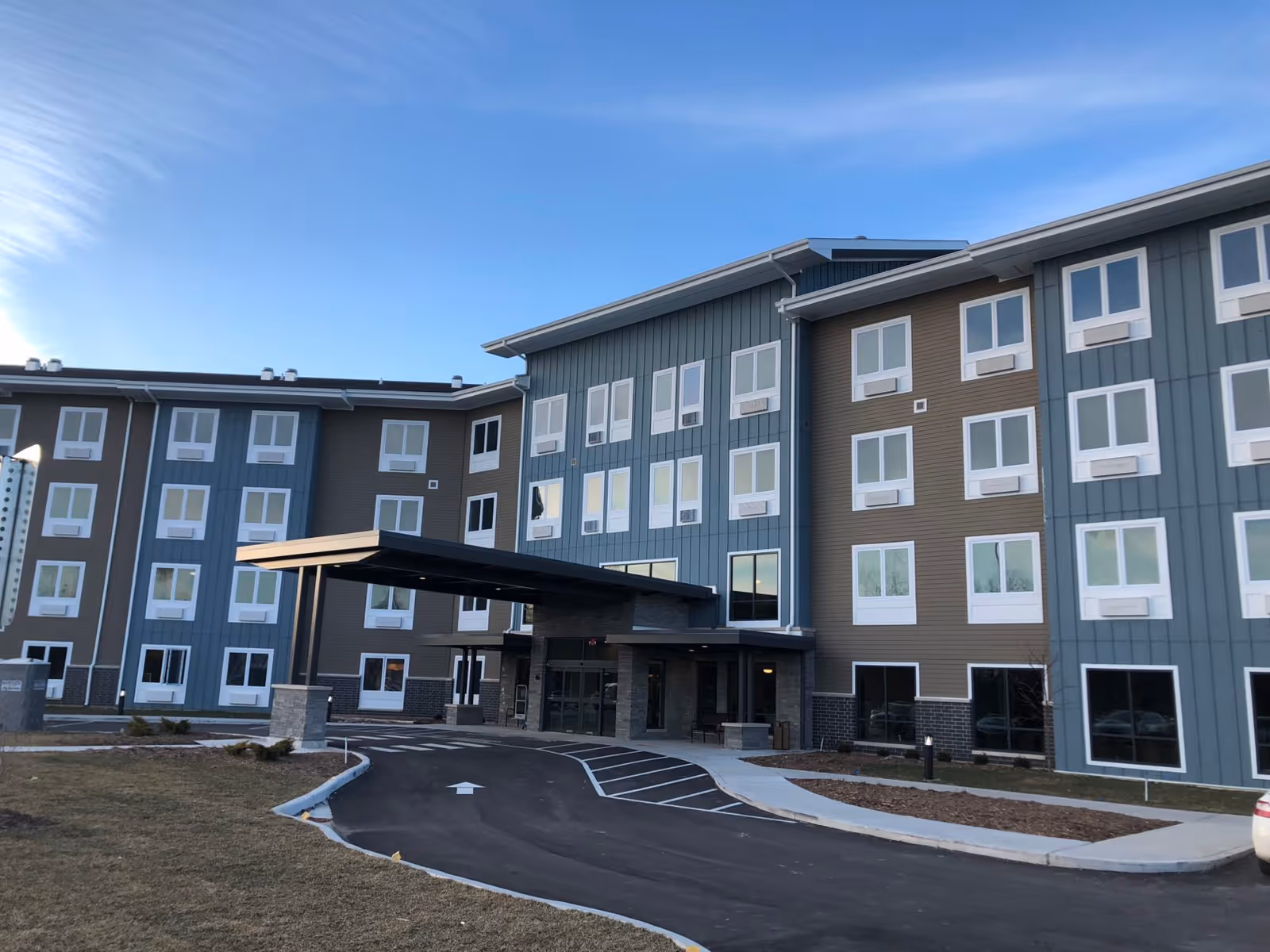 Exterior view of a modern multi-story senior living facility building with a covered entrance and multiple windows under a clear blue sky.
