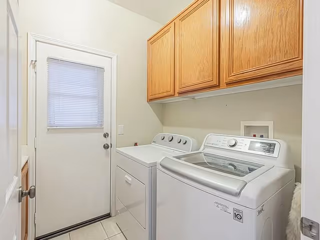 Laundry room with front-loading washer and top-loading dryer under wooden cabinets.