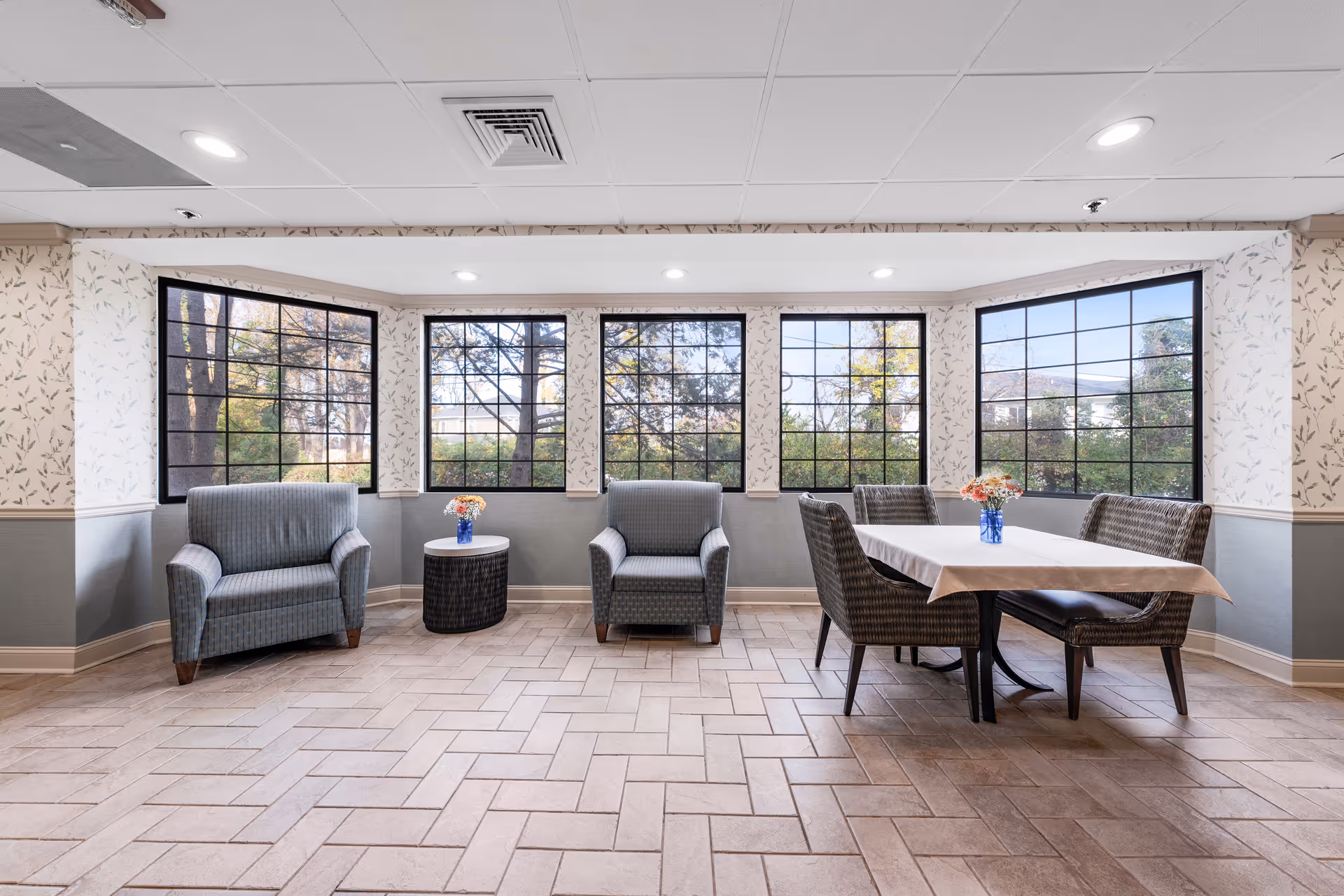 Bright lounge area with blue armchairs, a dining table, and large windows.