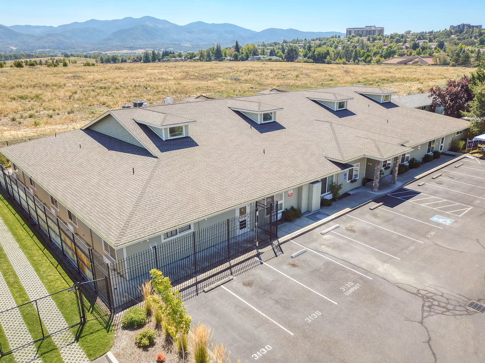 A single-story care facility with a sloped roof, parking lot, and fenced perimeter.