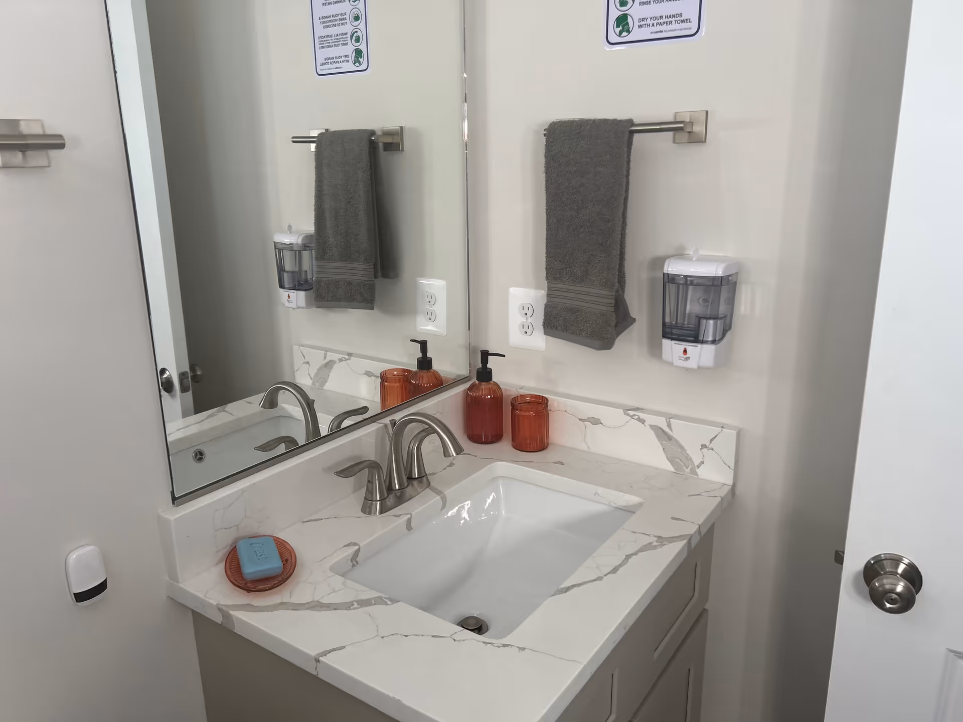 Modern bathroom sink area with marble countertop, towels, and dispensers in a senior facility.