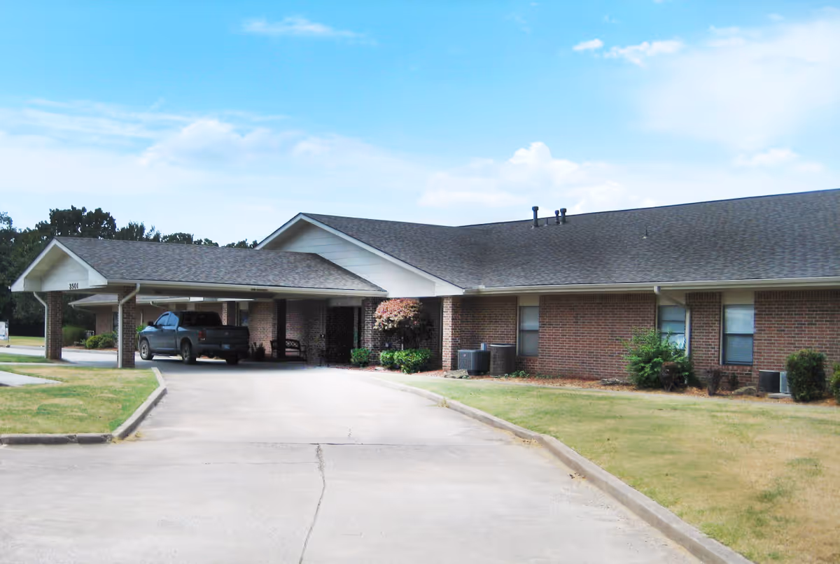 Single-story brick senior living facility exterior with a covered carport and parking.