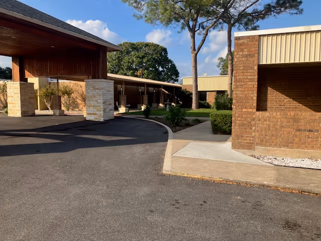 Entrance driveway and covered drop-off area of a brick senior living building with trees and walkways.