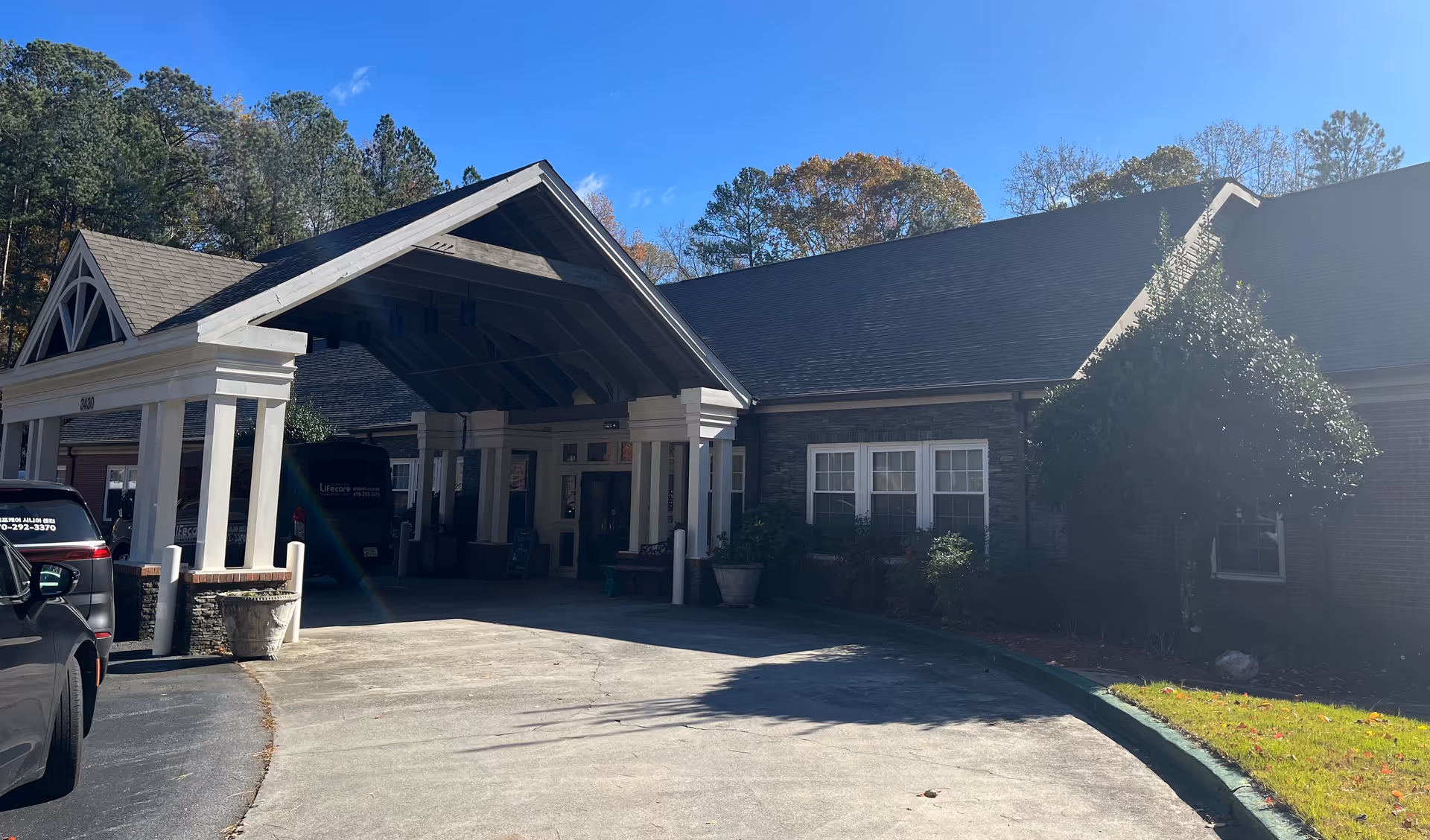 Entrance to Lifecare Partners senior living facility with covered drop-off area and parked cars.
