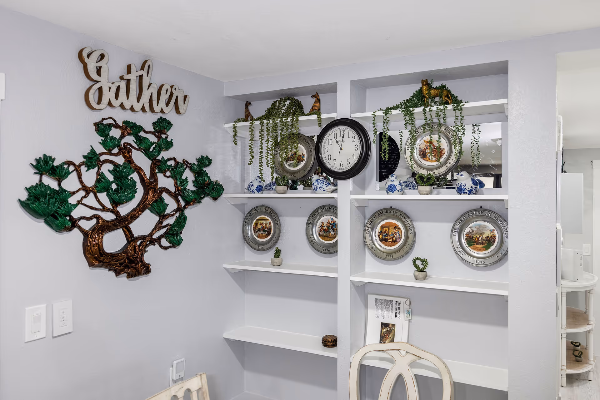 Light-gray wall features decorative tree art and shelves with plates.