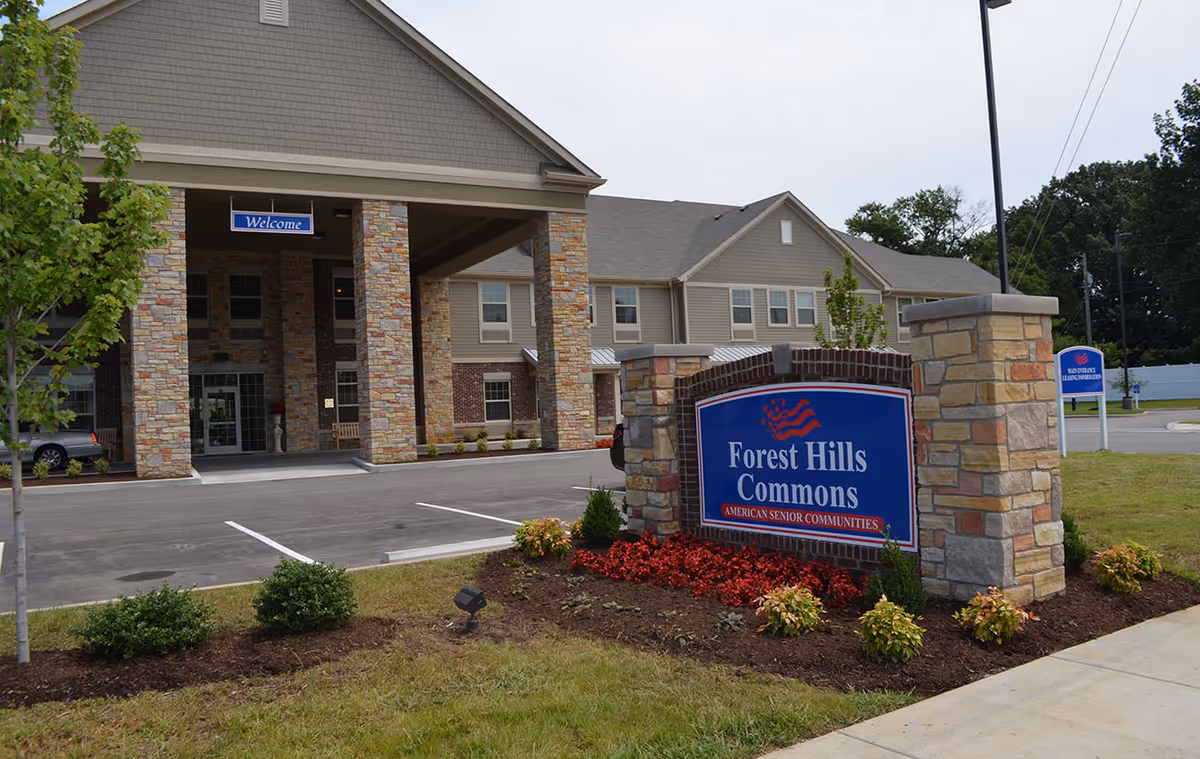 Exterior view of Forest Hills Commons entrance with stone columns, sign, and landscaped parking.