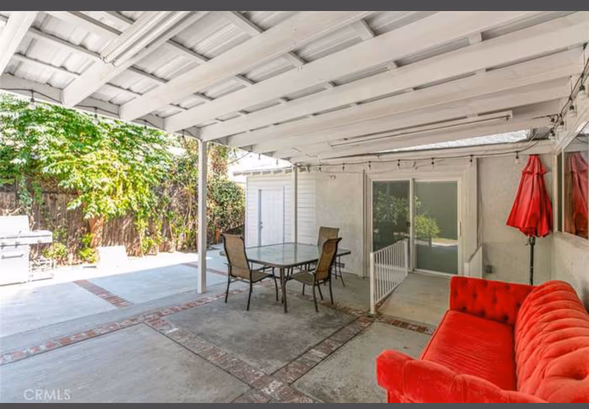 Covered outdoor patio with glass table, chairs, red sofa, and sliding door.