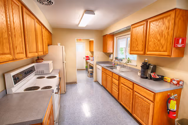 A long, bright galley kitchen with wooden cabinets, appliances, and a sink along counters.