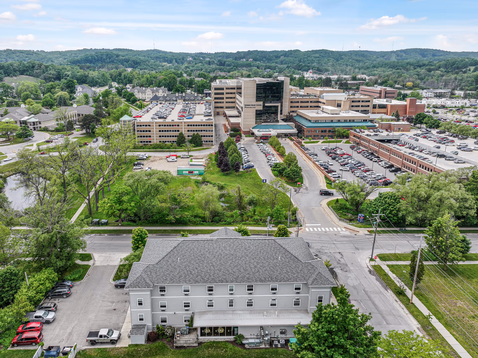 Aerial view of a senior living campus with a front building, parking lots, and green landscape.