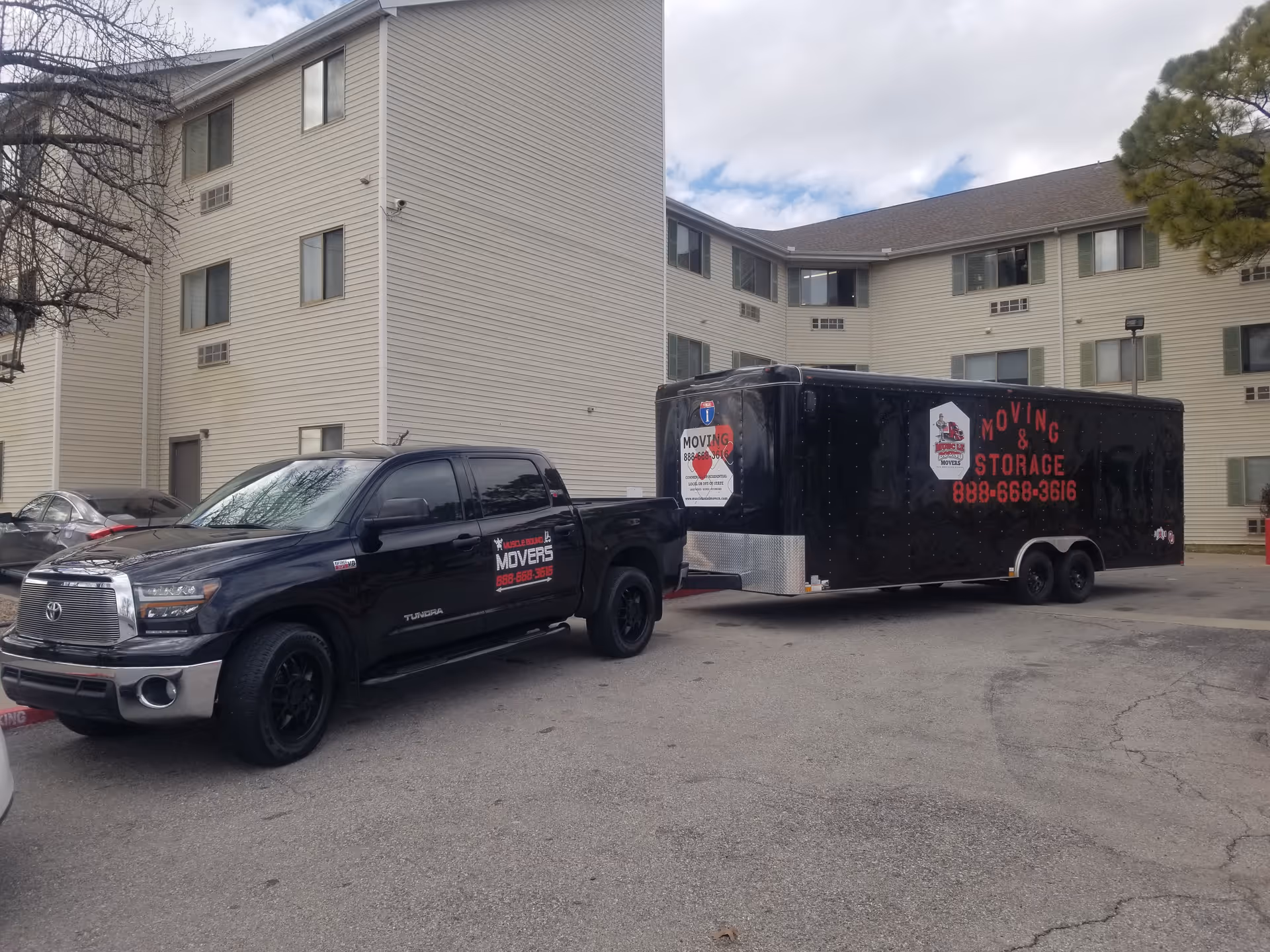 Three-story beige building exterior with a black moving truck and trailer parked outside.
