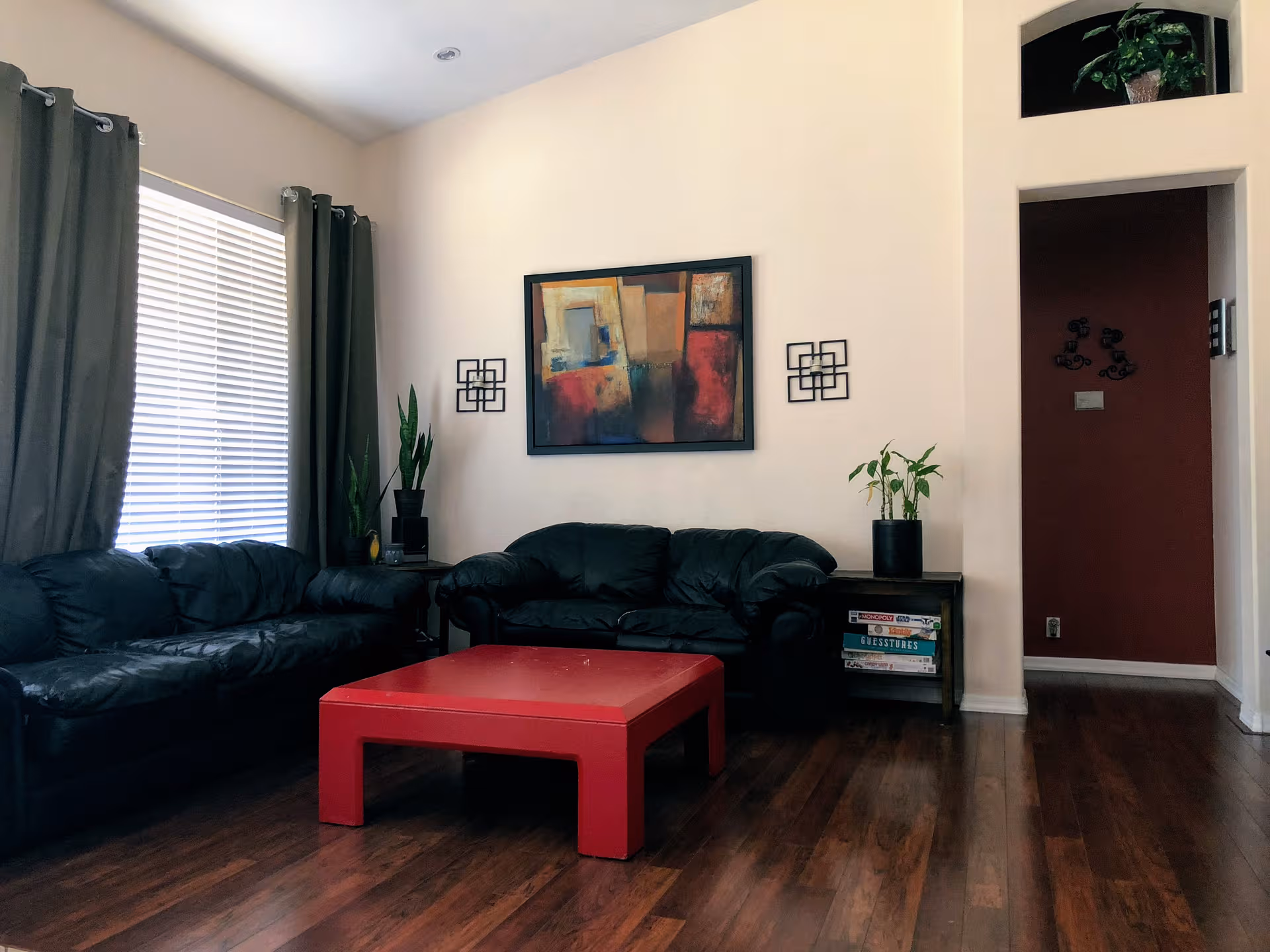 Living room with black leather sofas, a red coffee table, and potted plants