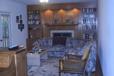 Cozy living room with a blue patterned sectional, fireplace, built-in bookshelves, and an armchair.