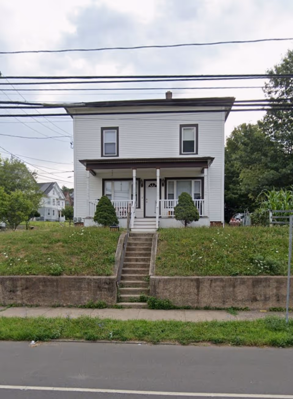 Two-story white house with a front porch, stairs, and power lines overhead.