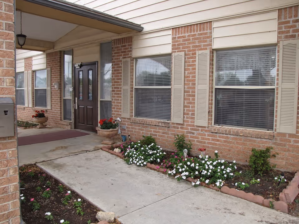 The brick building entrance at Bluebonnet Nursing and Rehabilitation features flower beds.