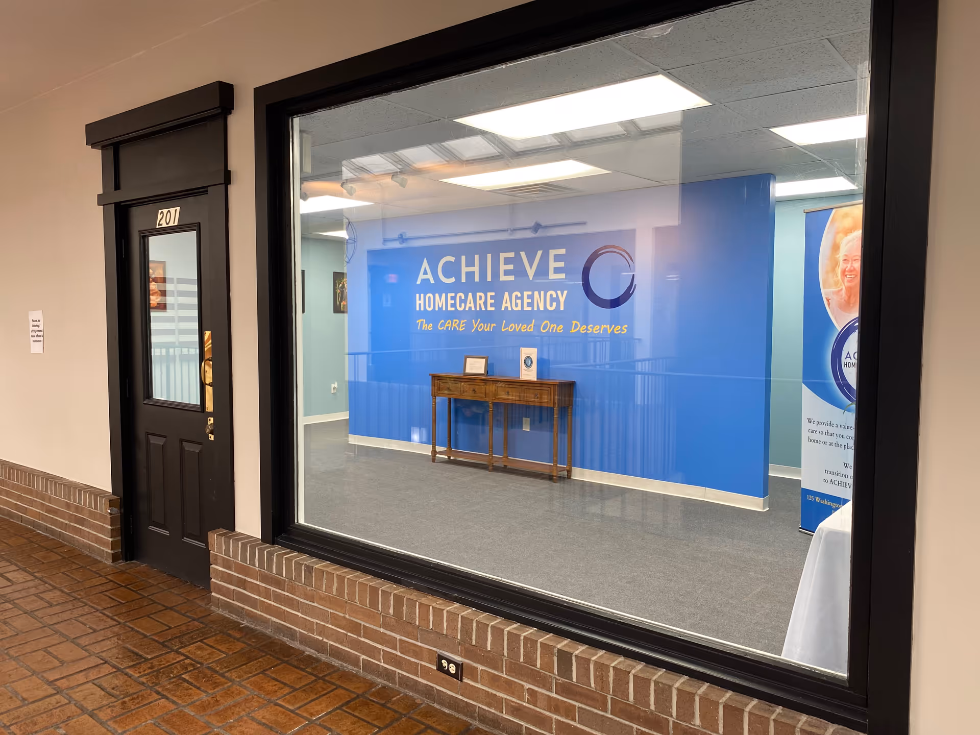 Inside hallway with blue ACHIEVE Homecare Agency wall and wooden console table.