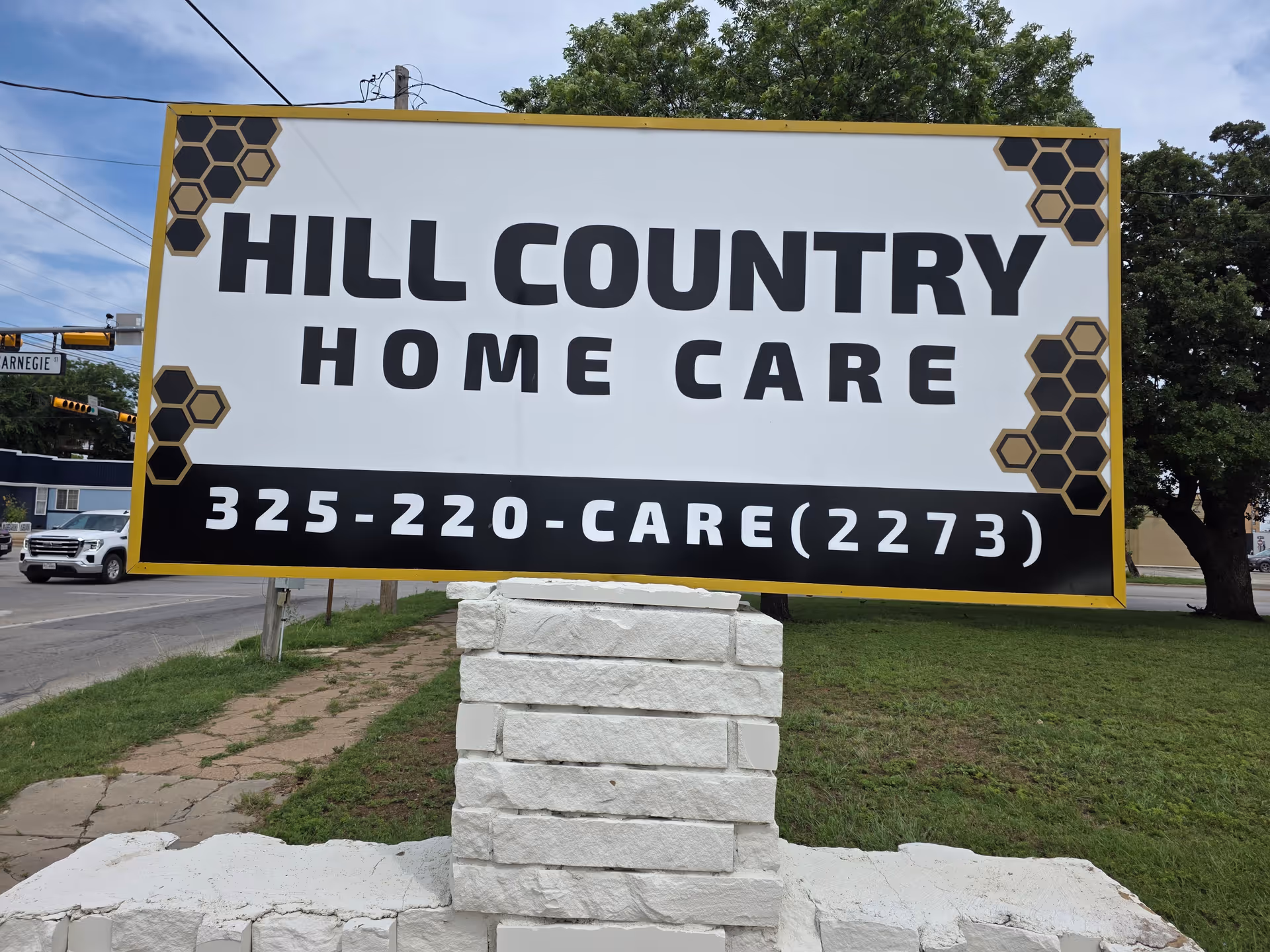 A large sign reading HILL COUNTRY HOME CARE sits on a stone base near the road.