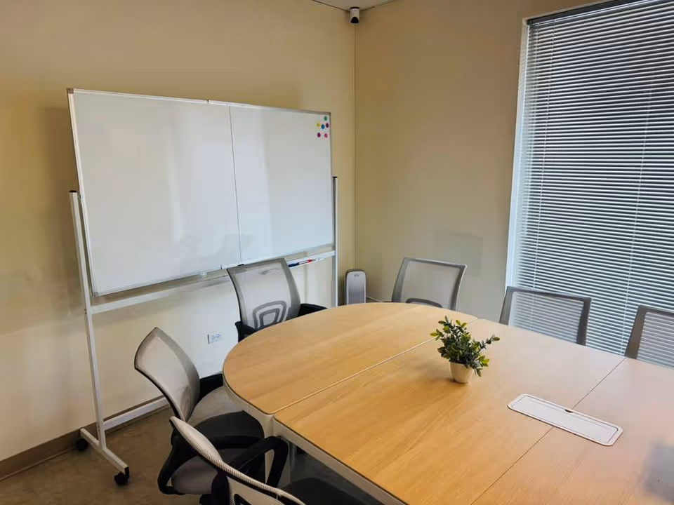 Round wooden conference table with chairs and a whiteboard in a bright office room.