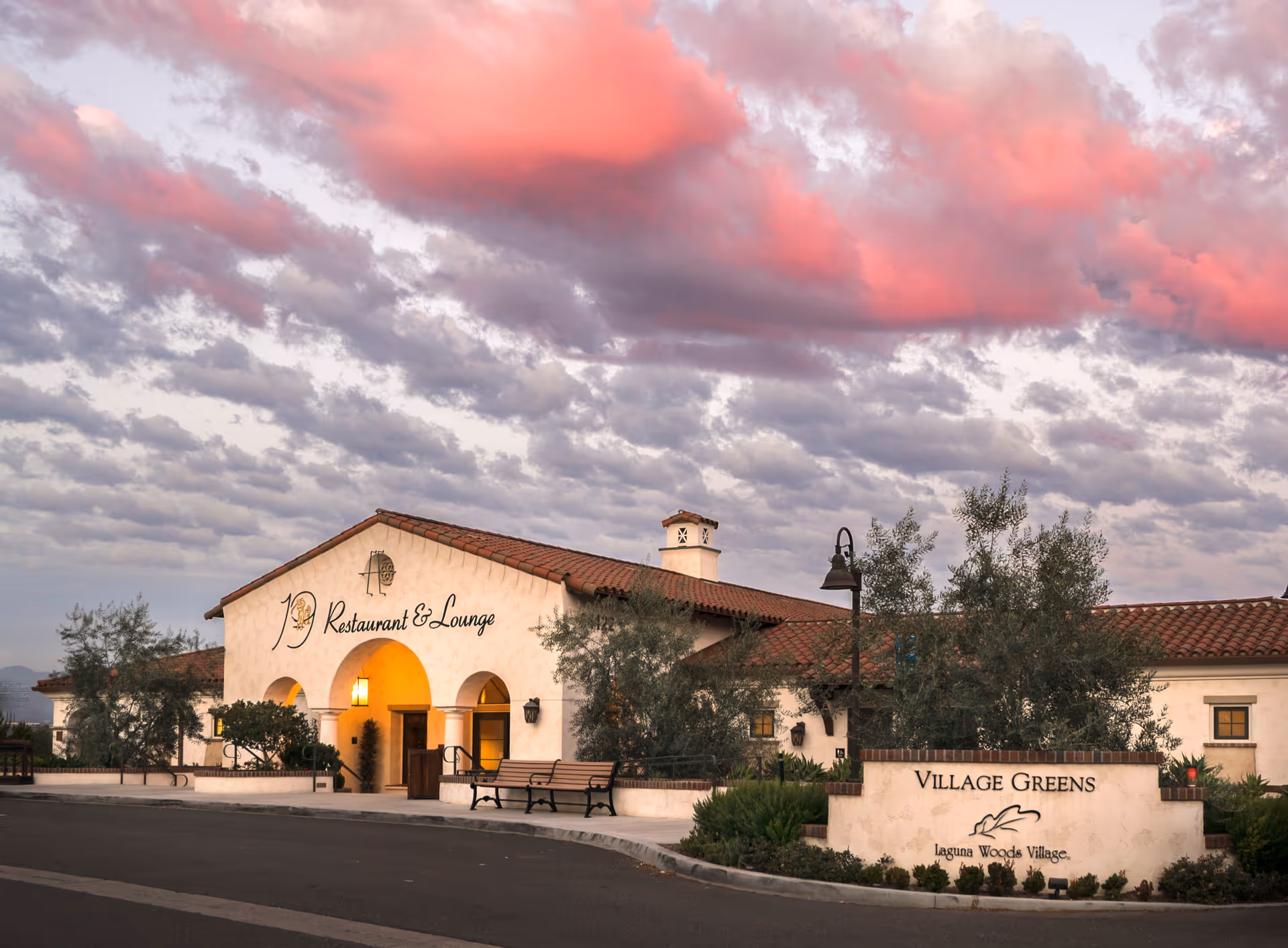 Exterior view of Laguna Woods Village building with Village Greens sign against a pink sunset