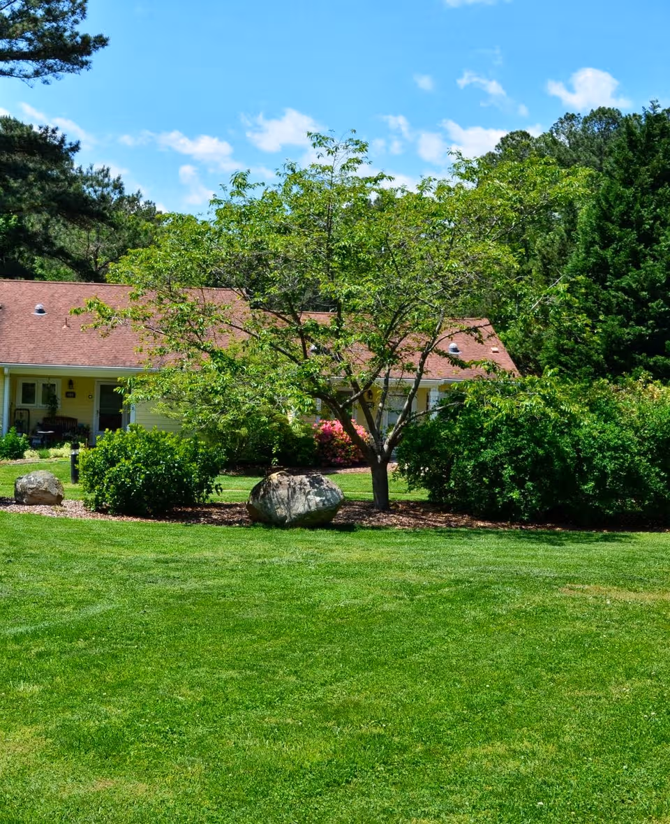 Lush lawn and trees surround a single-story building with a red sloped roof.