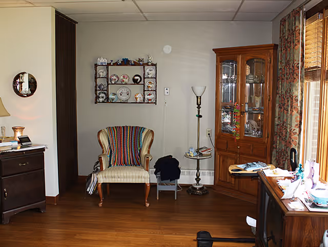Cozy living room in a senior facility with chairs, a cabinet, a desk, and decorations.