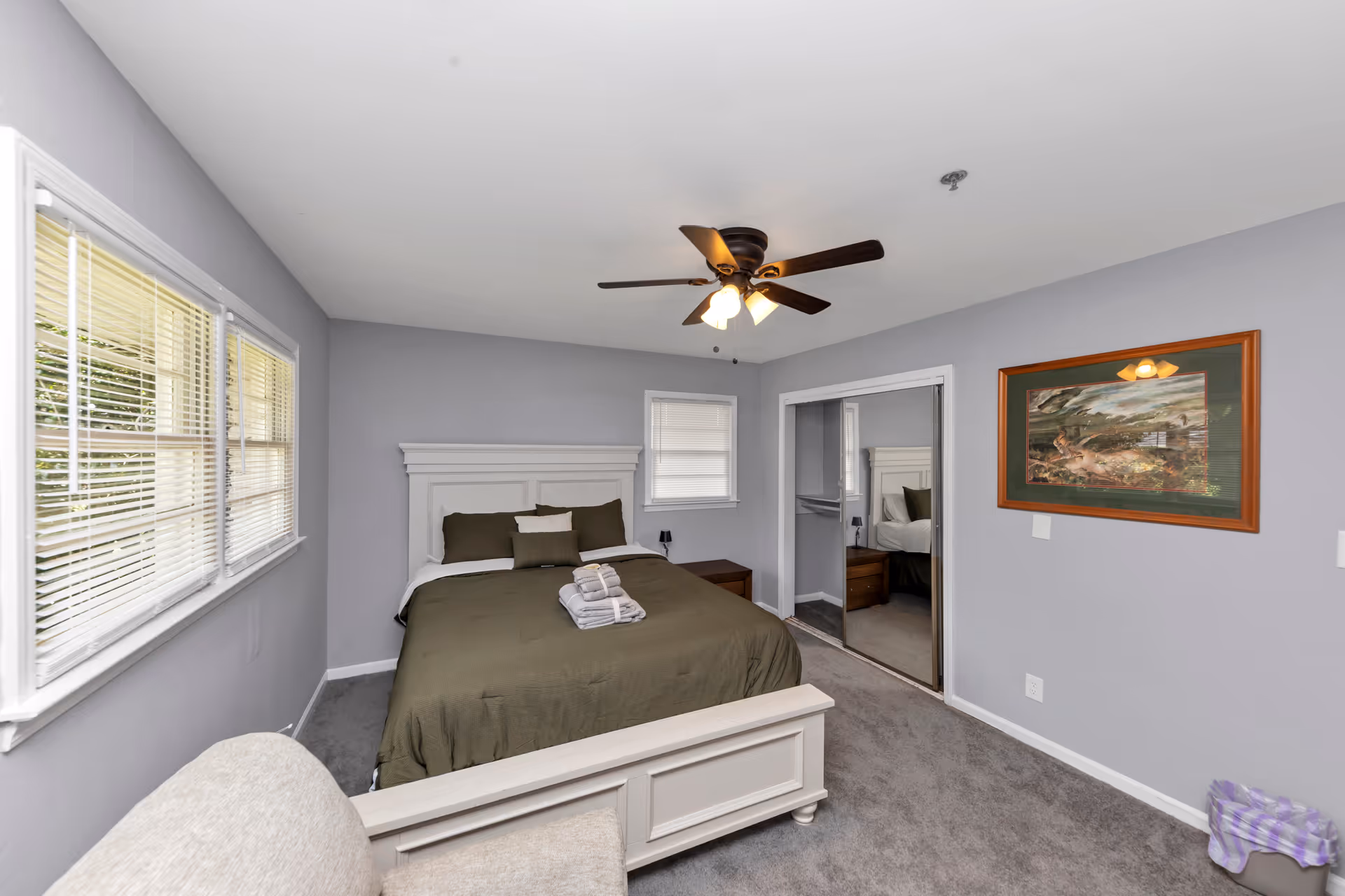 Senior living facility bedroom with bed, ceiling fan, windows, and mirrored closet.
