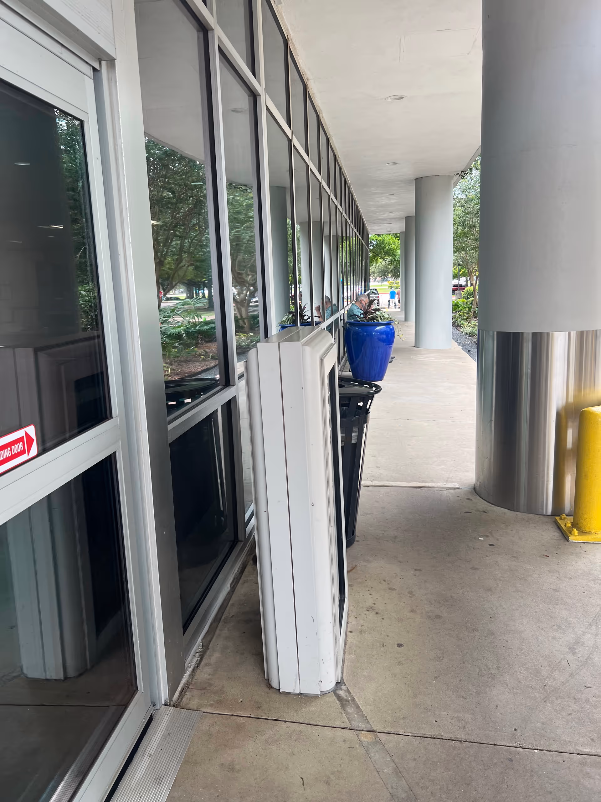 Exterior walkway along a building with large glass windows and columns.