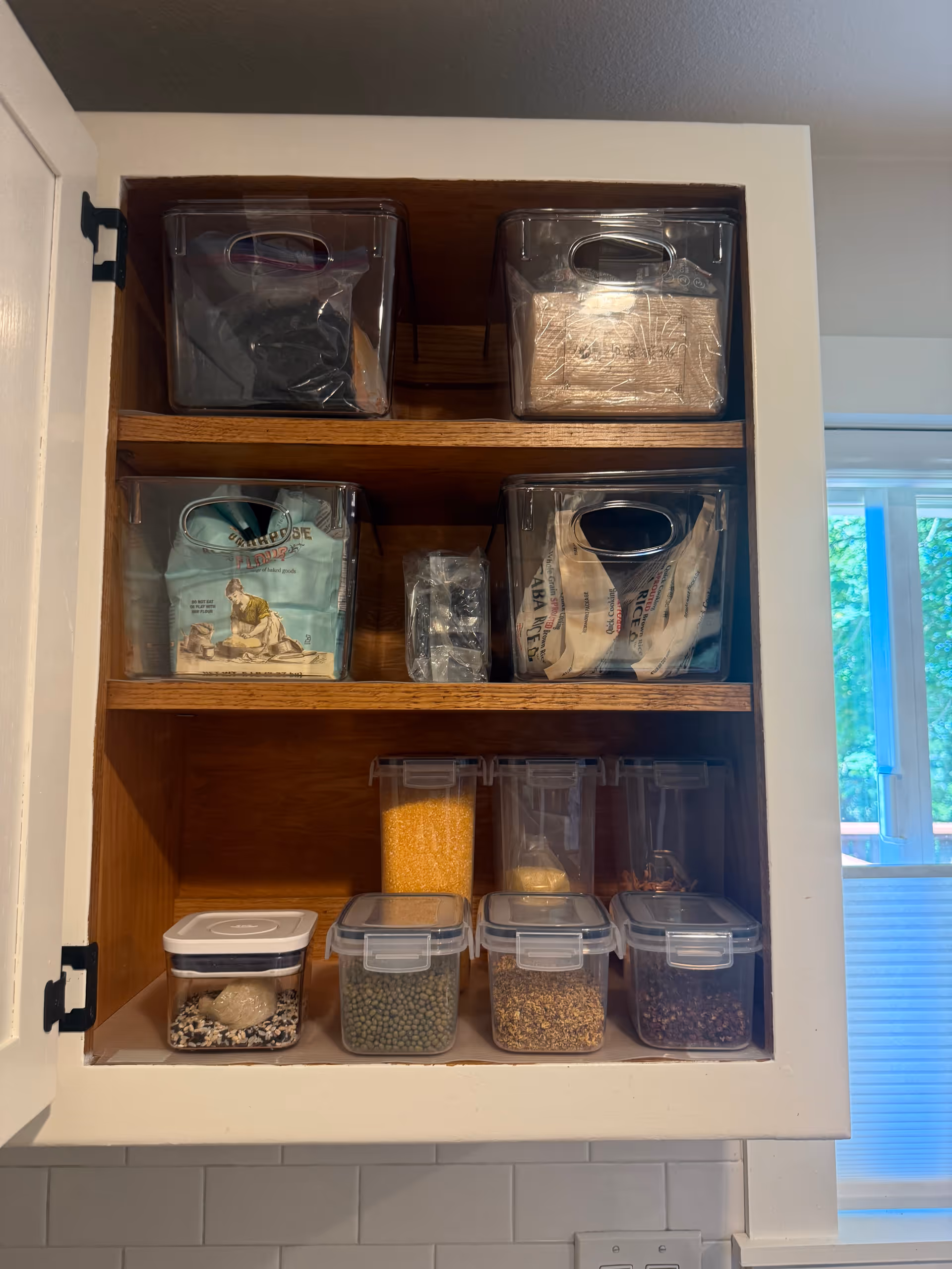Open kitchen cabinet with organized clear bins storing grains and pantry staples.