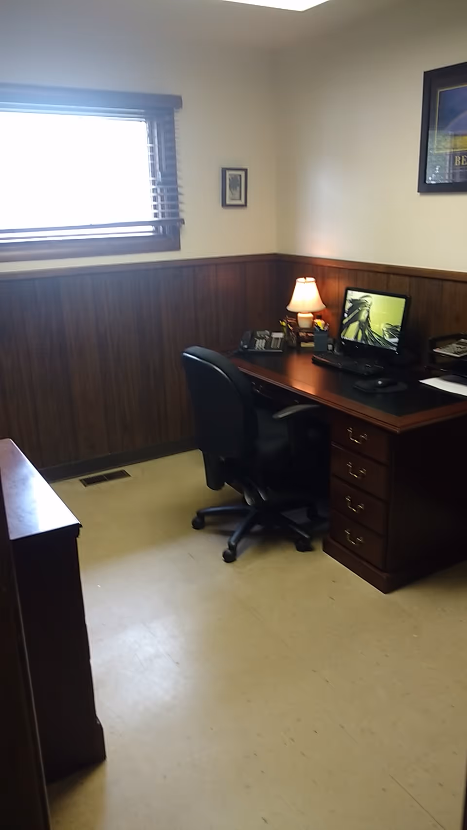 Office desk in a wood-paneled senior living facility with computer and lamp.