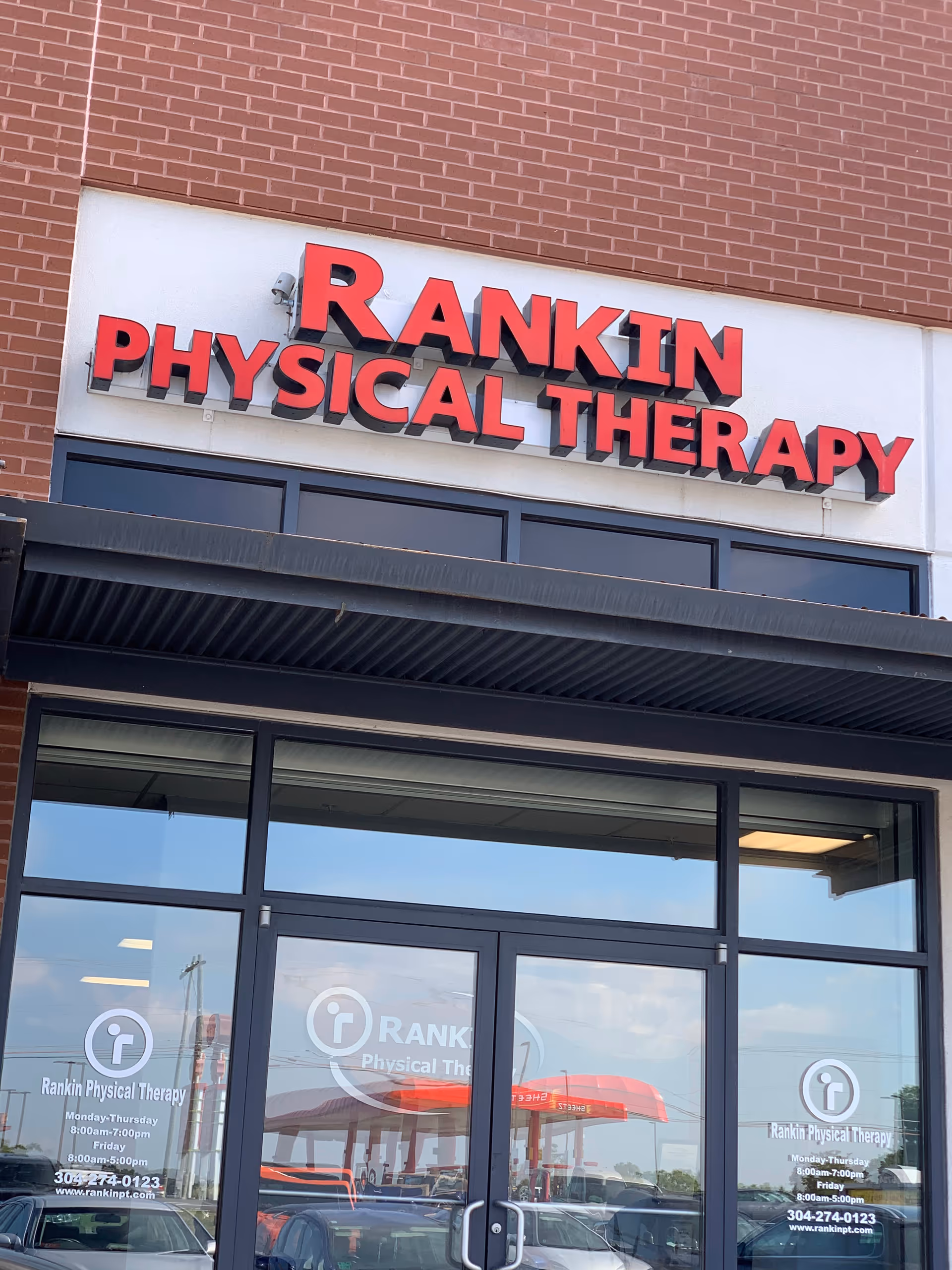 Brick storefront with Rankin Physical Therapy sign above glass doors and parking reflection.